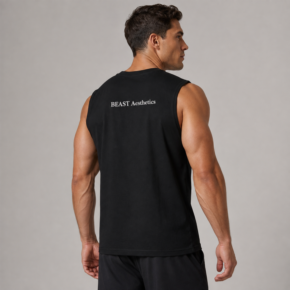 A muscular man shown from the back wearing a black sleeveless athletic tank top with 'BEAST Aesthetics' printed in white on the upper back, set against a plain gray studio background.