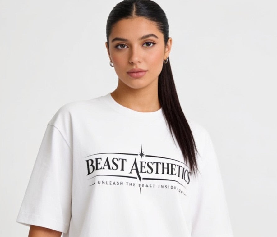 A woman with dark hair in a ponytail wearing a white oversized t-shirt with a black graphic print that reads 'BEAST AESTHETICS' and 'UNLEASH THE BEAST INSIDE'.