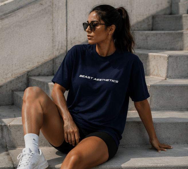 A woman wearing a navy blue t-shirt with 'BEAST AESTHETICS' printed in white across the chest, sitting on concrete outdoor stairs.