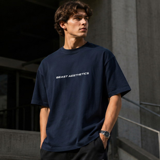 A man wearing a navy blue crewneck t-shirt with 'BEAST AESTHETICS' printed in white across the chest, standing outdoors against a concrete building.