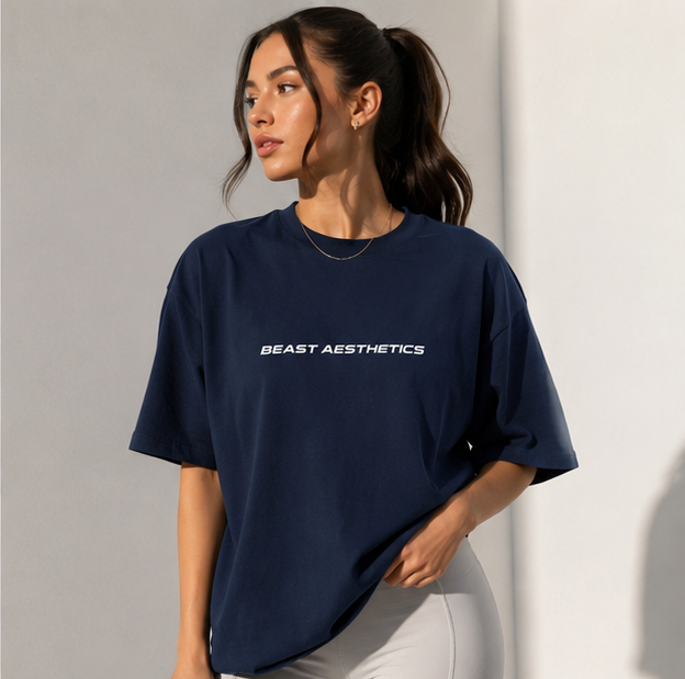 A woman wearing an oversized navy blue t-shirt with 'BEAST AESTHETICS' printed in white across the chest, paired with light gray leggings, set against a minimalist gray background.