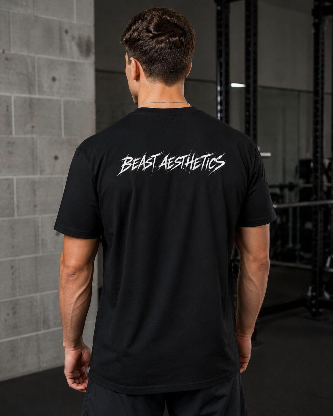 A man viewed from behind wearing a black t-shirt with 'BEAST AESTHETICS' printed in white across the upper back, set in a gym environment.
