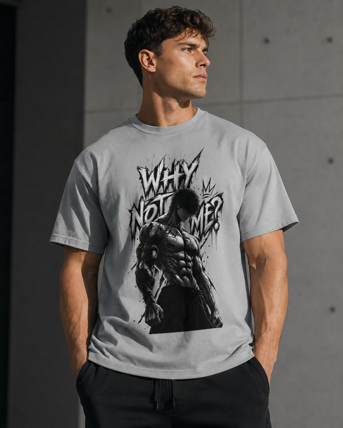 A man wearing a light gray graphic t-shirt with a black and white print of a muscular man and the text 'WHY NOT ME?' against a concrete wall background.