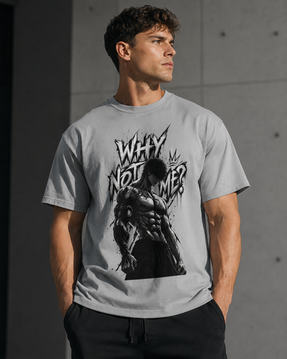 A man wearing a light gray graphic t-shirt with a black and white print of a muscular man and the text 'WHY NOT ME?' against a concrete wall background.