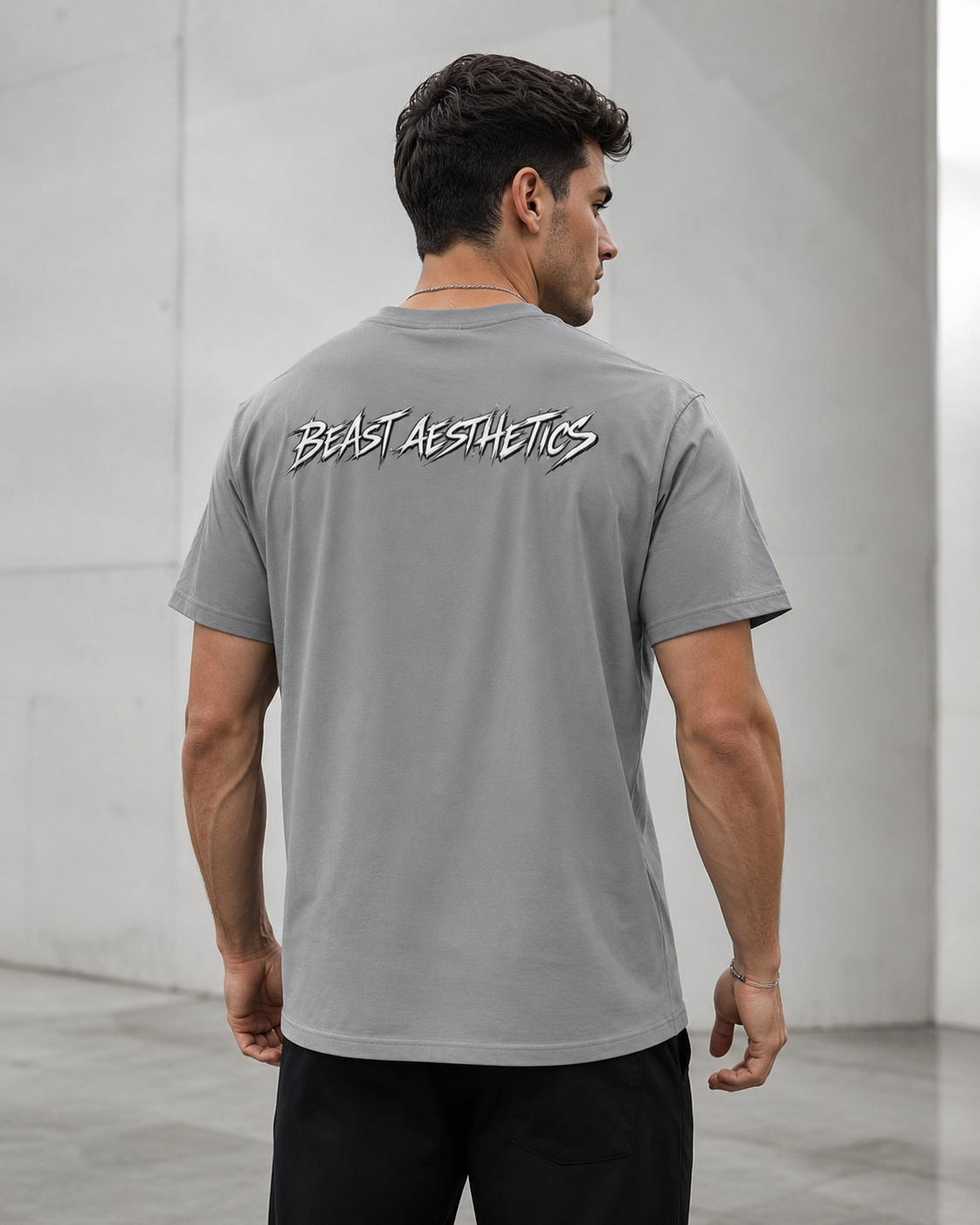 A man viewed from behind wearing a gray t-shirt with 'BEAST AESTHETICS' printed in white across the upper back, set against a minimalist concrete wall background.