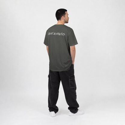 A man stands with his back to the camera wearing a dark gray t-shirt with 'BASE AESTHETICS' printed in white across the upper back, paired with black cargo pants and white sneakers, against a plain light gray studio background.