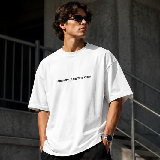 A man wearing a white oversized t-shirt with 'BEAST AESTHETICS' printed in black across the chest, standing outdoors in front of concrete stairs and railings.