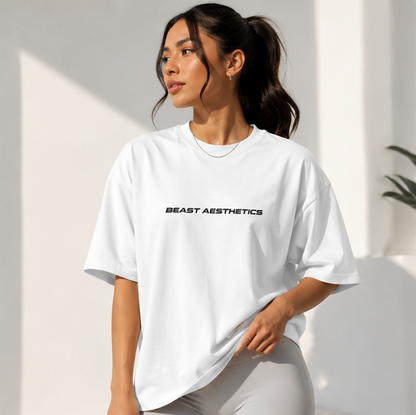 A woman wearing a white oversized T-shirt with 'BEAST AESTHETICS' printed in black across the chest, paired with light gray leggings, posed in bright, sunny white walls.