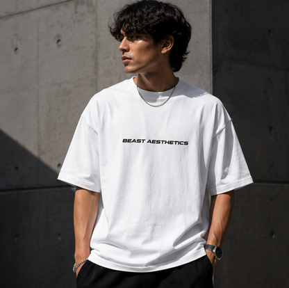 A man wearing a white short-sleeve t-shirt with 'BEAST AESTHETICS' printed in black across the chest, standing against a textured concrete wall.