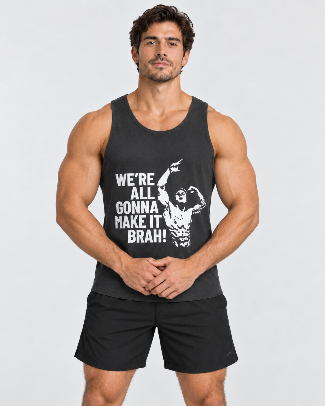 A muscular man modeling a black tank top with a white graphic text that reads 'WE'RE ALL GONNA MAKE IT BRAH!' and a flexing muscular figure, paired with black athletic shorts, against a light gray background.
