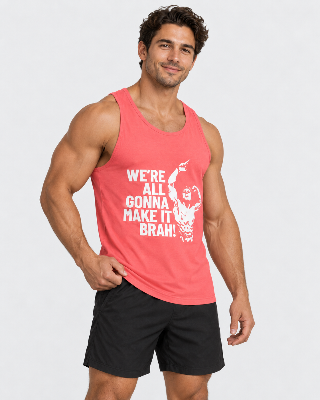 A muscular man wearing a coral pink tank top with a white graphic print that reads 'WE'RE ALL GONNA MAKE IT BRAH!' and black athletic shorts, posed against a light gray studio background.