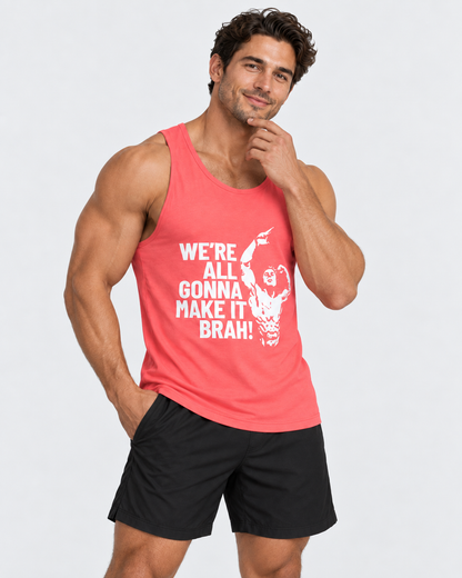 A muscular man wearing a coral pink tank top with a white graphic print that reads 'WE'RE ALL GONNA MAKE IT BRAH!' and black athletic shorts, posing against a light gray studio background.