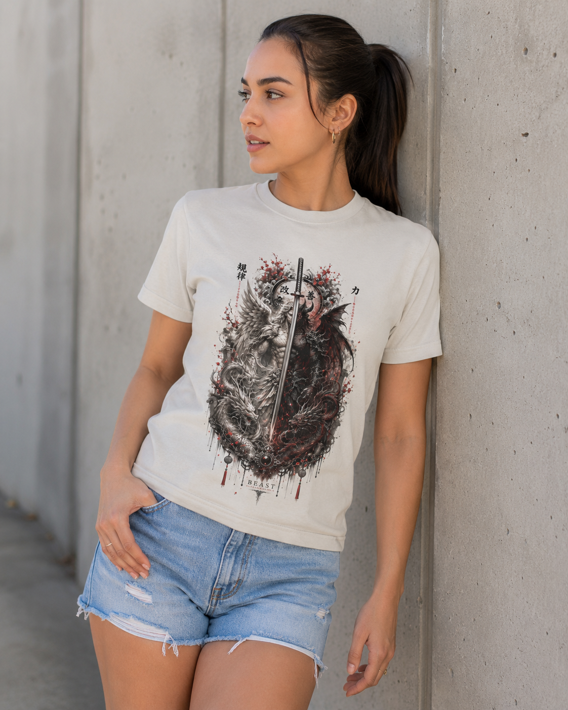 A woman wearing a white graphic t-shirt with a detailed black and red wolf design, paired with light blue denim shorts, leaning against a concrete wall.