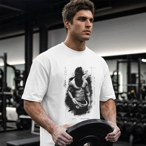 A man in a gym wearing a white t-shirt with a black graphic print of a muscular man, holding a barbell. The background shows gym equipment.