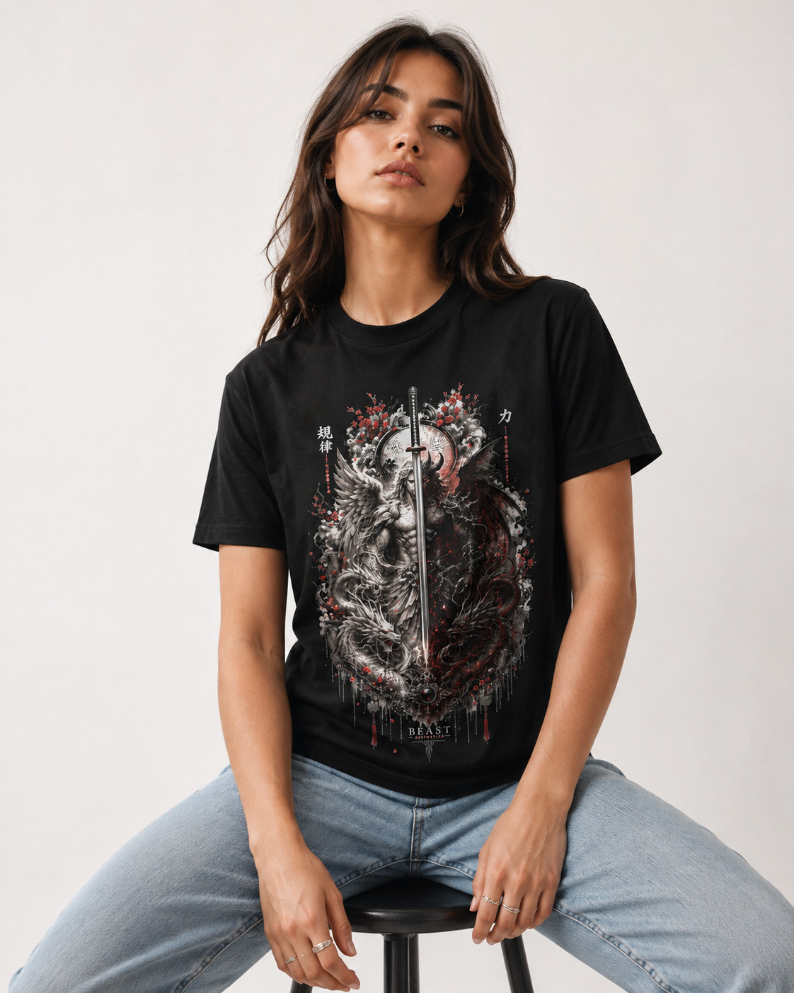 A woman wearing a black graphic t-shirt with a detailed dragon design, seated on a stool against a plain light background.