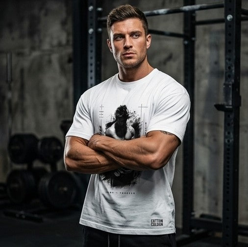A muscular man in a gym wearing a white graphic t-shirt with a black print of a bodybuilder and the text 'GUTTON FITNESS'.