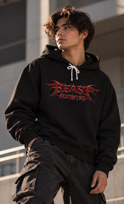 A man wearing a black hoodie with a red and black 'BLAST AESTHETICS' graphic on the chest, paired with dark cargo pants, standing outdoors against a modern concrete building.