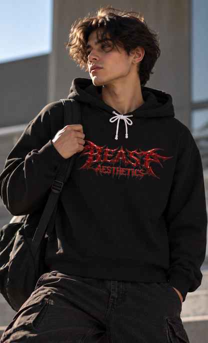 A man wearing a black hoodie with a red 'BEAST AESTHETICS' graphic on the chest, styled with black cargo pants and a black backpack, set against a modern concrete background.