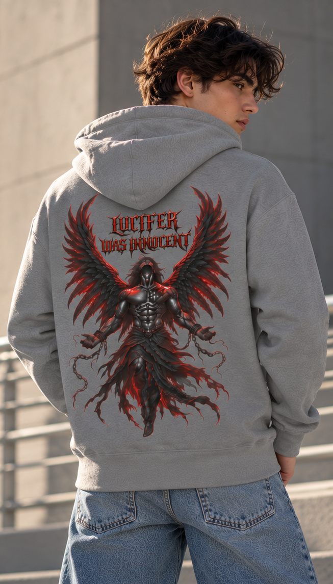 A person wearing a light gray hoodie from the back, featuring a large graphic print of a winged demon-like figure with red flames and the text 'LUCIFER WAS DEVIL' in red. The person is also wearing light blue jeans, standing outdoors against a concrete wall.