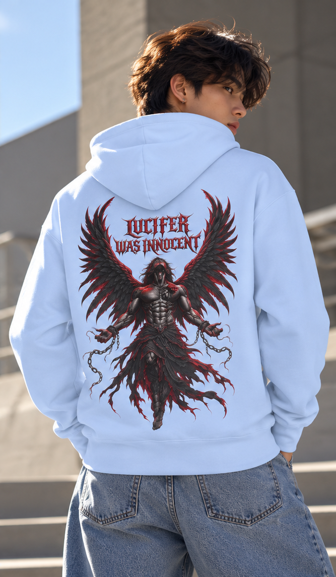A person wearing a light blue hoodie from the back, featuring a large graphic print of a winged demon with the text 'LUCIFER WAS INNOCENT' in red. The person is also wearing blue jeans, standing outdoors against a gray concrete wall.