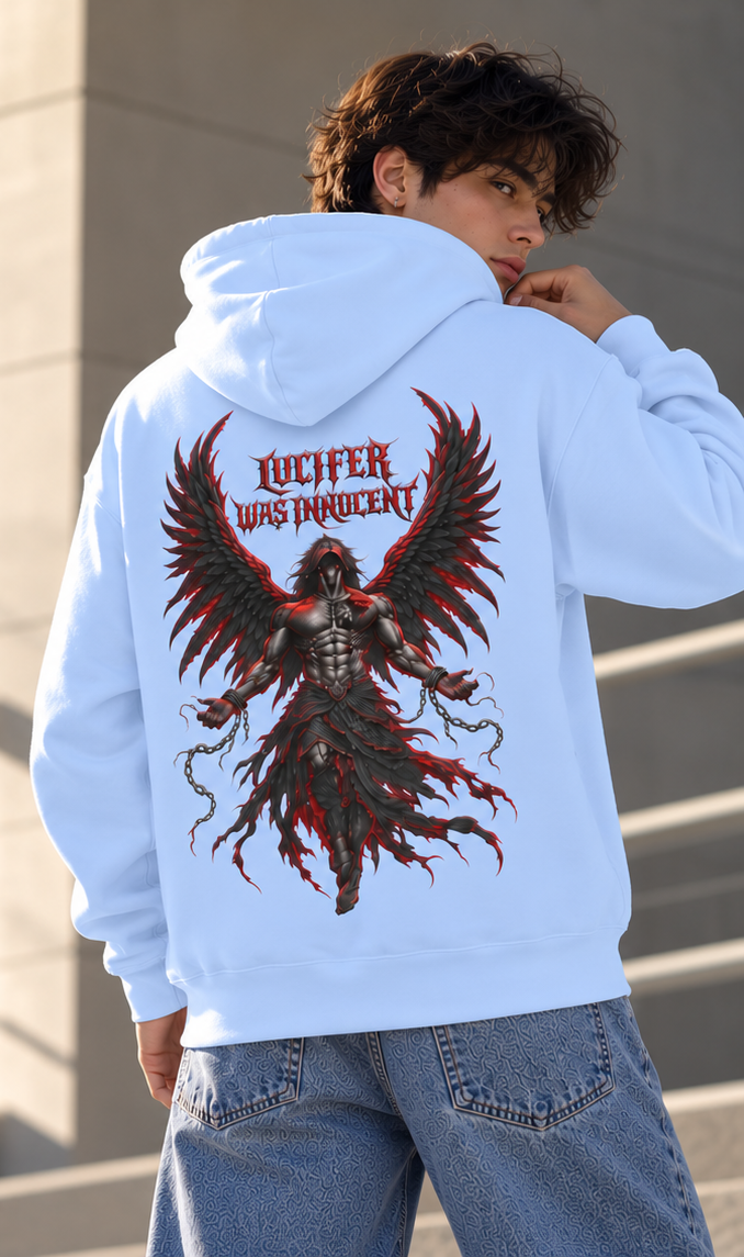 A man wearing a light blue hoodie from the back, featuring a large graphic of a dark angel with red wings and the text 'LUCIFER WAS IMPENitent' in red. He is also wearing blue jeans, standing against a neutral concrete wall.