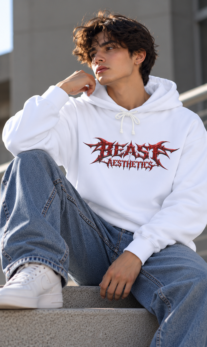 A young man sitting on concrete steps wearing a white hoodie with a red gothic-style 'BEAST AESTHETICS' graphic, paired with blue jeans and white sneakers.