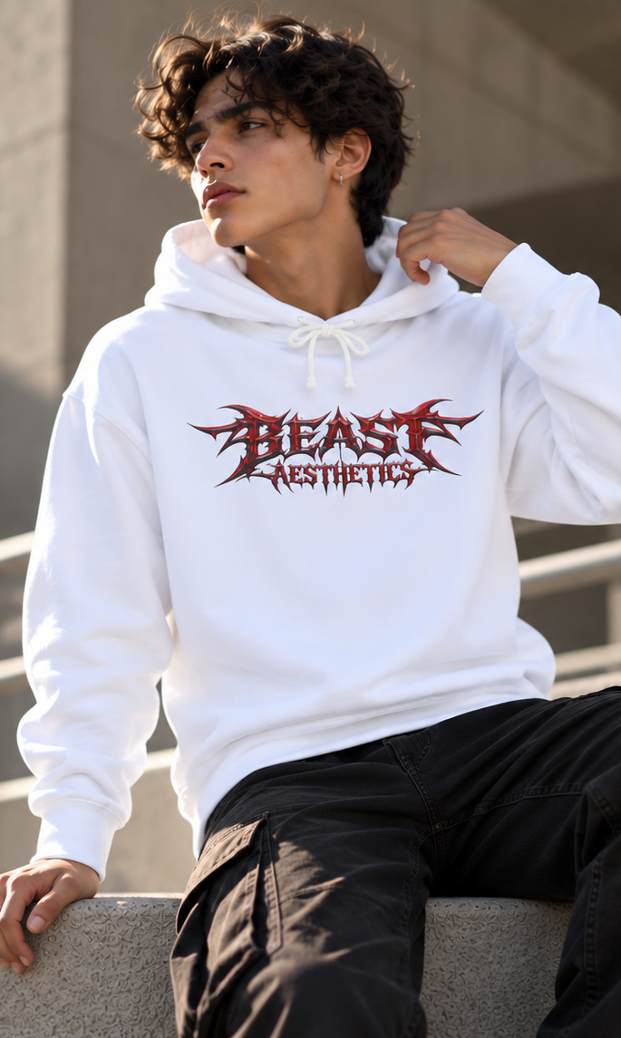 A man wearing a white pullover hoodie with a red and black 'BEAST AESTHETICS' graphic on the chest, paired with black cargo pants, sitting on a concrete ledge.