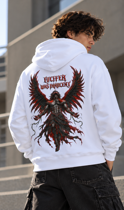 A person wearing a white hoodie from the back, featuring a large graphic print of a dark winged figure and the text 'LUCIFER WAS PROHIBITED' in red. The person is standing outdoors against a modern building background.
