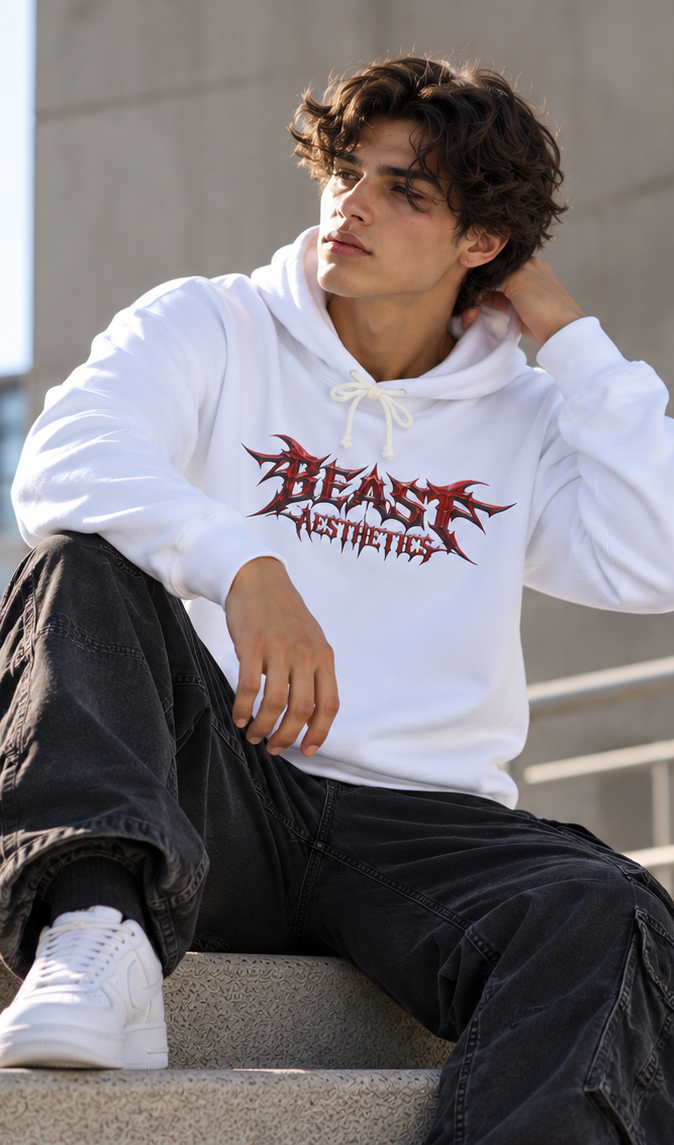 A man wearing a white pullover hoodie with a red and black 'BEAST AESTHETICS' graphic, paired with black cargo pants and white sneakers, sitting on concrete steps.